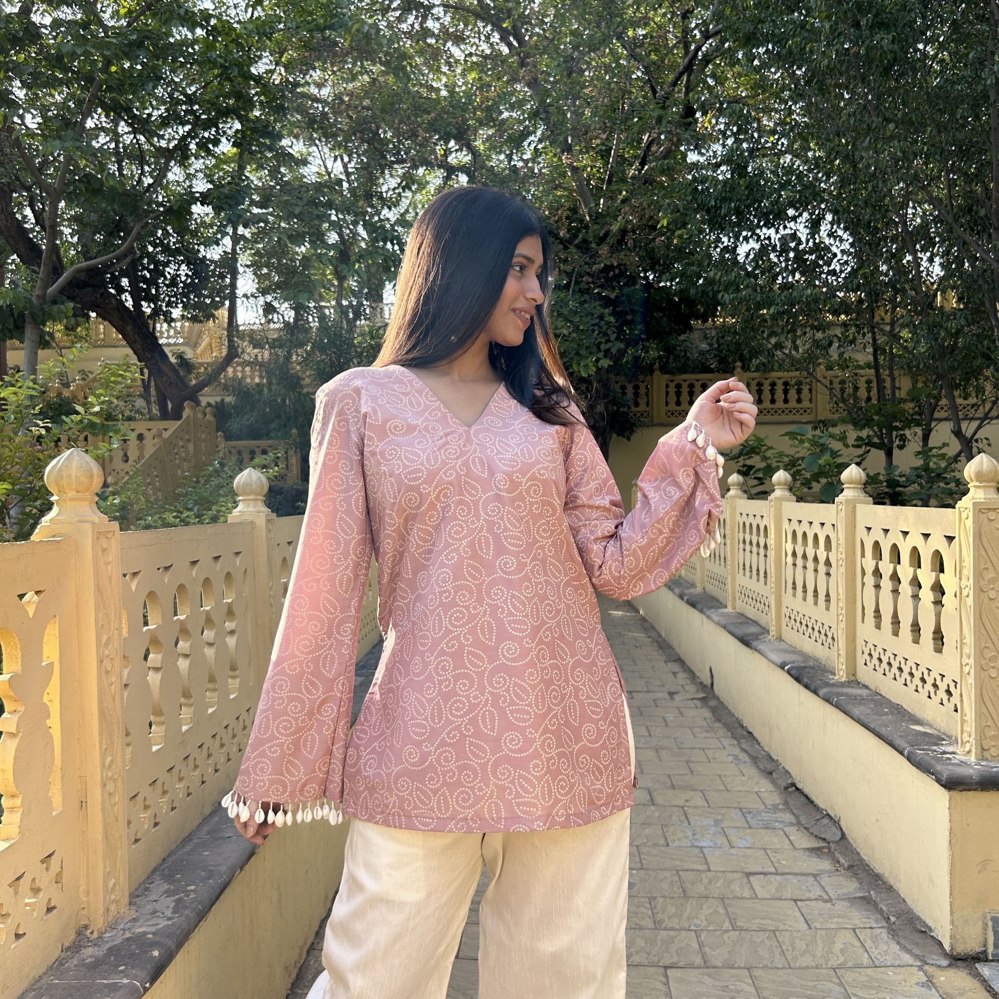 Pink printed short kurta with V-neckline and shell pearl sleeves, paired with white pants
